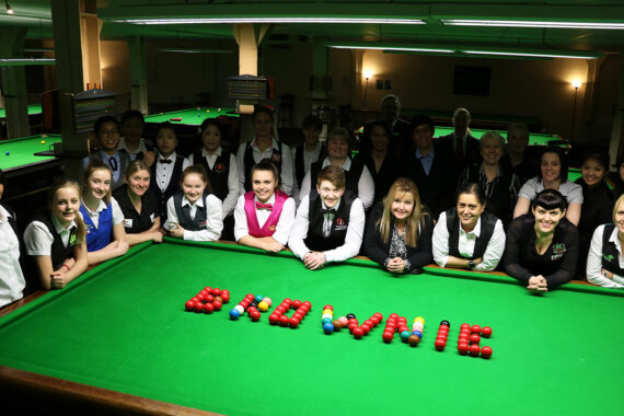 Group of players stood next to snooker table with balls shaped to say 'Brownie'