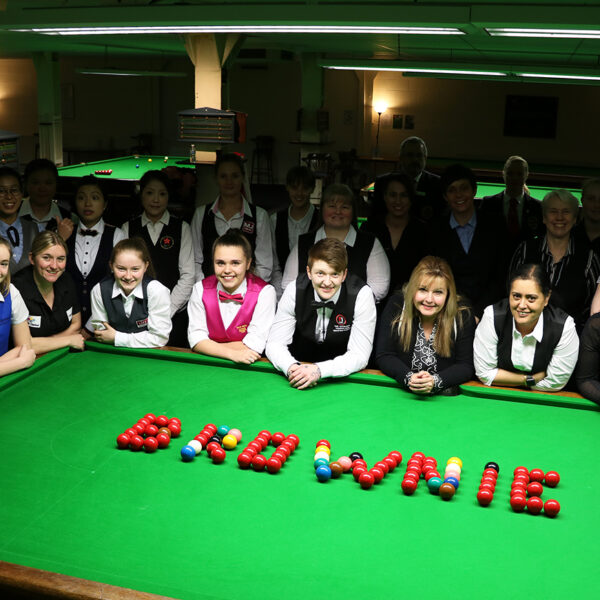 Group of players stood next to snooker table with balls shaped to say 'Brownie'