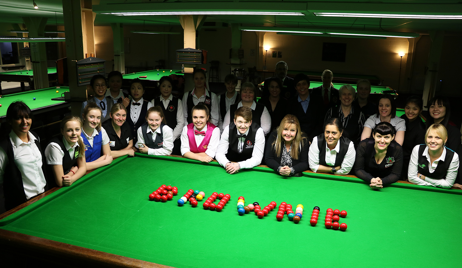 Group of players stood next to snooker table with balls shaped to say 'Brownie'